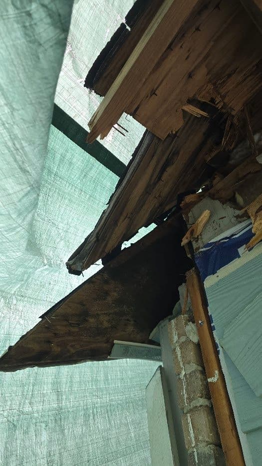 Damaged wooden roof section covered by tarpaulin, showing rot and wear.