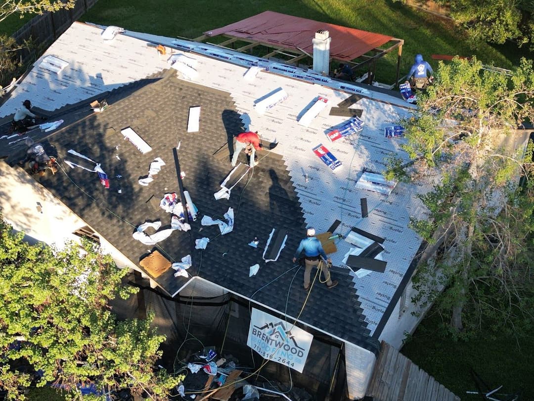 Roof being installed by workers on a residential property with construction materials visible.