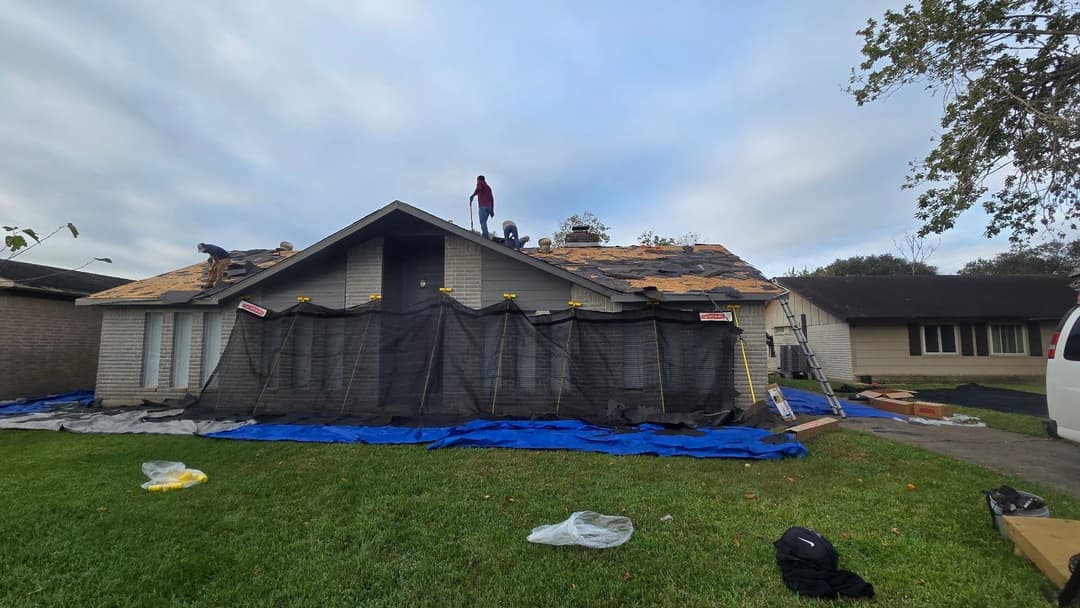 Workers installing a new roof on a house with tarps and scaffolding.