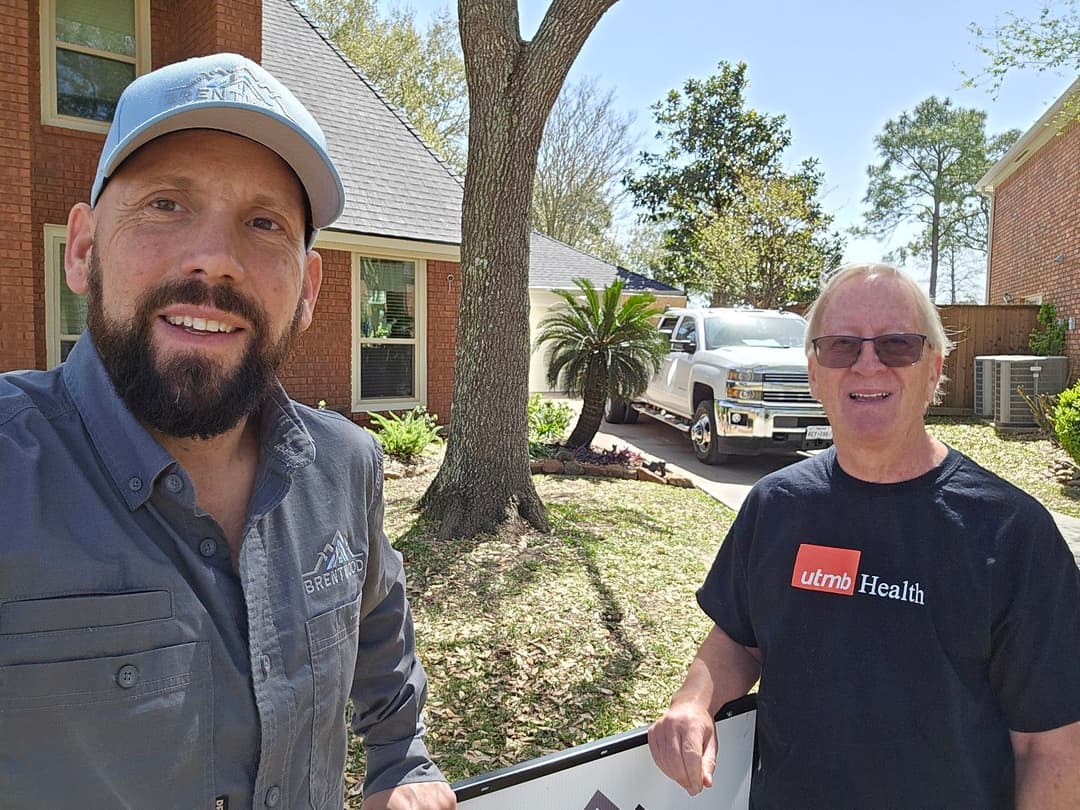 Two men pose outside a house with a truck in the background, promoting a local service.