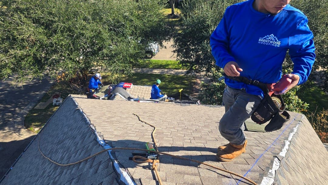 Roofers working on a residential roof, with safety gear and tools visible.
