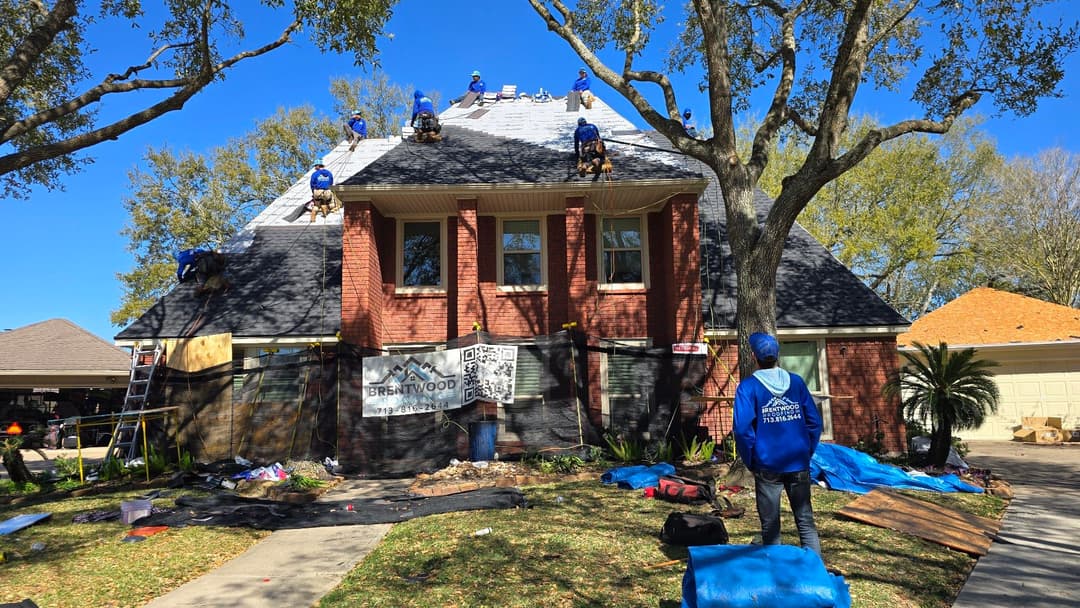 Roofing crews install new shingles on a residential home under clear blue skies.
