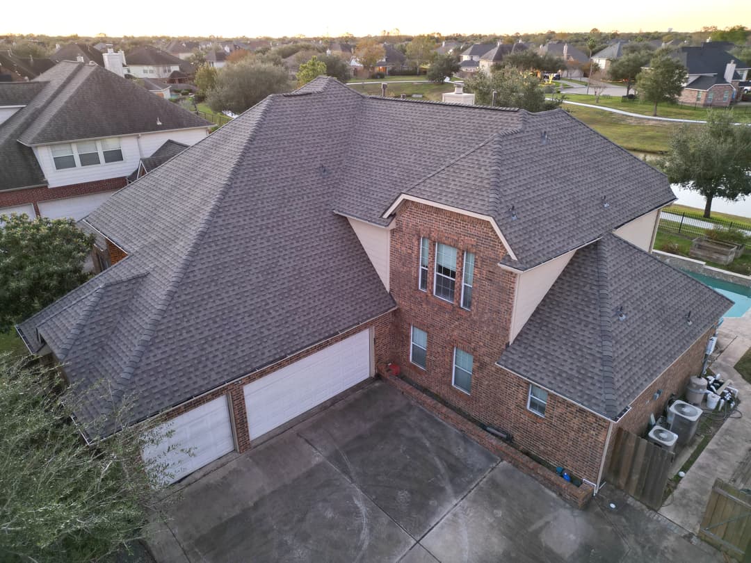Aerial view of a modern two-story brick house with a gray shingled roof and driveway.