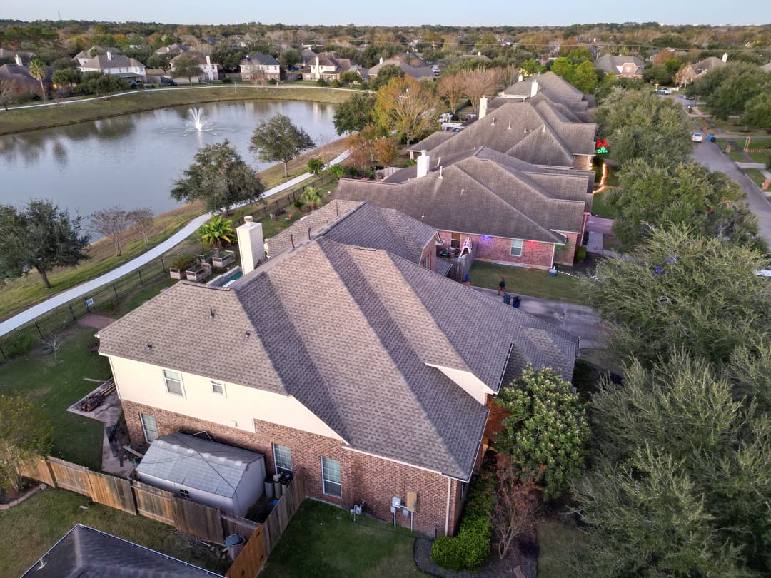 Aerial view of suburban homes beside a serene pond with trees and walking path.