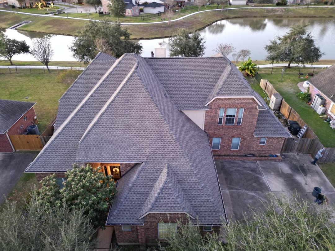 Aerial view of a two-story brick home near a pond, showcasing a well-maintained roof.
