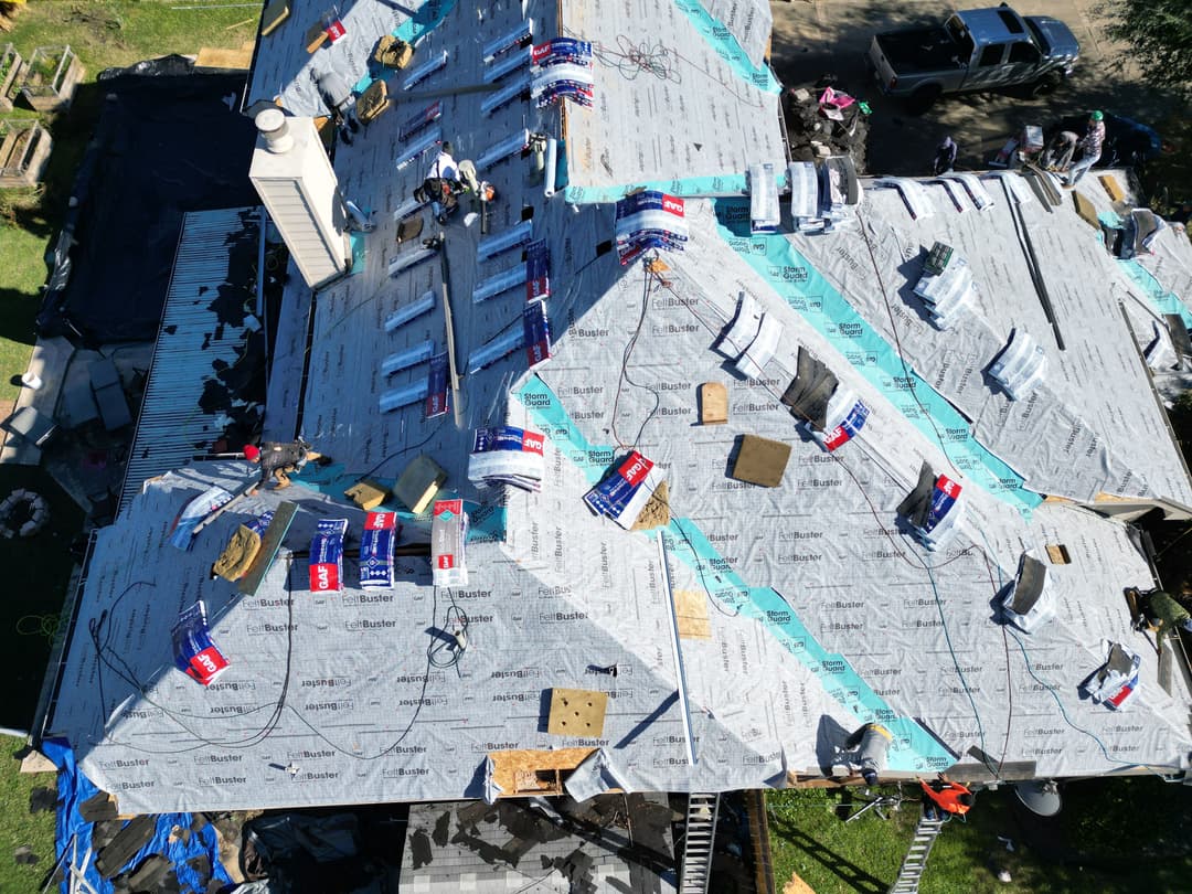 Aerial view of a house under roof renovation with materials and workers on the roof.