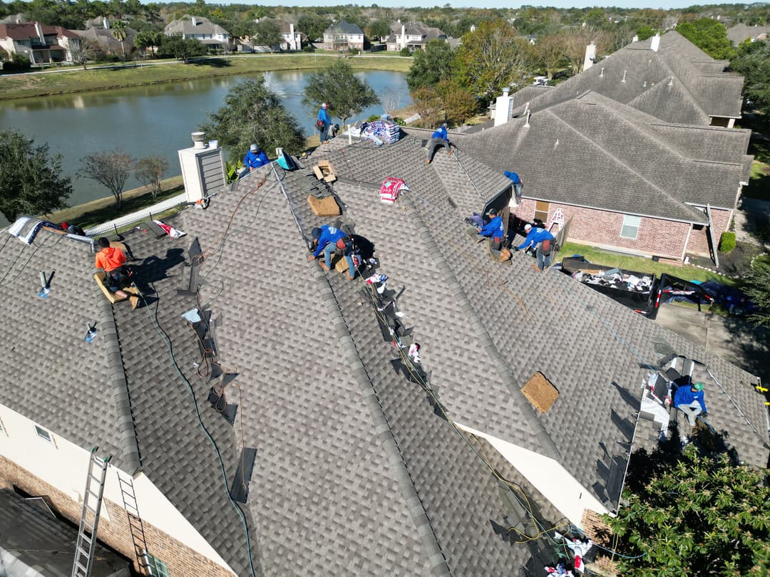Roofing crew repairing a residential roof near a lake on a sunny day.