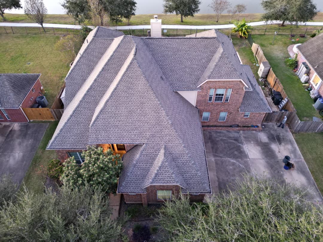 Aerial view of a stylish brick home with a well-maintained roof and landscaped yard.